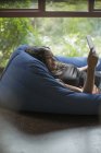 Щаслива молода жінка розслабляється з цифровим планшетом у кріслі для мішків — стокове фото