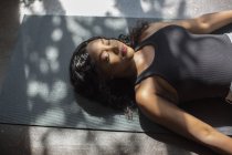 Serena giovane donna posa in posa cadavere su tappetino di yoga soleggiato — Foto stock