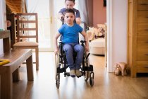 Мальчик толкает брата с синдромом Дауна в инвалидной коляске — стоковое фото
