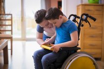 Boy with Down Syndrome using digital tablet in wheelchair — Stock Photo