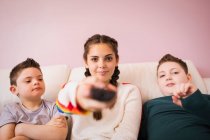 Portrait confident girl with remote control watching TV with brothers — Stock Photo