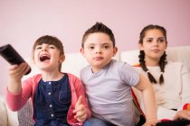 Down Syndrome siblings watching TV on sofa — Stock Photo