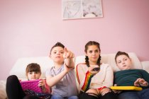 Мальчик с синдромом Дауна смотрит телевизор с братьями и сестрами на диване — стоковое фото