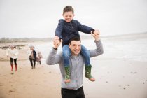 Portrait playful father carrying son on shoulders on winter beach — Stock Photo