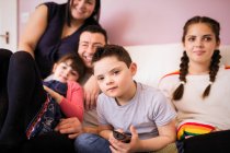 Porträt Junge mit Down-Syndrom vor dem Fernseher mit Familie auf dem Sofa — Stockfoto