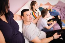 Portrait homme heureux regardant la télévision sur canapé avec la famille — Photo de stock