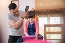Отец расчесывает волосы дочери с помощью цифровой таблетки — стоковое фото