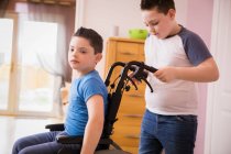 Niño empujando hermano con síndrome de Down en silla de ruedas - foto de stock