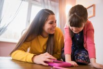 Щасливі сестри використовують цифровий планшет за столом — стокове фото
