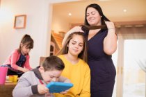 Famille fixant les cheveux et en utilisant une tablette numérique dans la salle à manger — Photo de stock