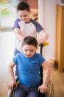 Мальчик толкает брата с синдромом Дауна в инвалидной коляске — стоковое фото