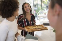 Felice giovane donna che serve pizza fatta in casa ad amici in cucina — Foto stock