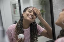 Glückliche junge Frau trägt Feuchtigkeitscreme im Badezimmerspiegel auf — Stockfoto