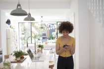 Giovane donna freelance utilizzando smart phone in cucina — Foto stock