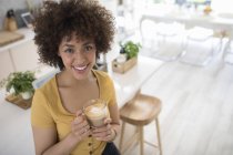 Portrait happy young woman drinking cappuccino in kitchen — Stock Photo