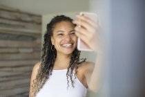 Feliz mujer joven que se toma el pelo con el teléfono de la cámara - foto de stock