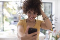 Уверенно улыбающаяся молодая женщина делает селфи с телефоном — стоковое фото