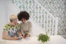 Young women friends using smart phones in kitchen — Stock Photo