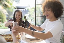 Glückliche junge Frau schenkt Wein für Freundin am Tisch ein — Stockfoto