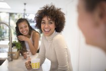 Happy young women friends laughing and drinking tea in kitchen — Stock Photo