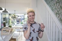 Smiling hembra freelance hablando por teléfono inteligente en cocina. - foto de stock