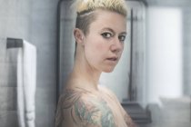 Selbstbewusste Frau mit Tätowierungen und nackten Schultern im Badezimmer — Stockfoto