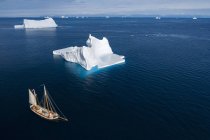 Navio que navega através de icebergs no oceano azul ensolarado Groenlândia — Fotografia de Stock