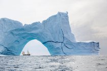 Корабль, плывущий за величественной айсбергской аркой на Атлантическом океане — стоковое фото