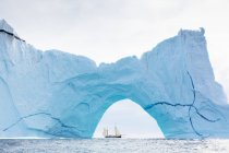 Schiff segelt hinter majestätischem Eisbergbogen auf Atlantik Grönland — Stockfoto
