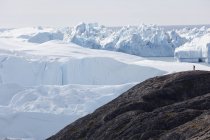 Hombre en acantilado con vistas a los majestuosos glaciares polares Groenlandia - foto de stock