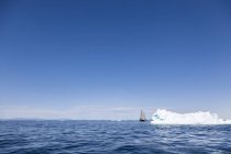 Barco navegando detrás del iceberg en el soleado océano Atlántico azul Groenlandia - foto de stock