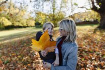 Retrato madre e hijo con hoja de otoño en un parque soleado. - foto de stock