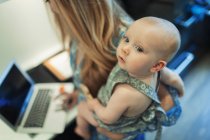 Mother working at laptop and holding cute baby daughter — Stock Photo