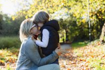 Mãe afetuosa e filho abraçando no parque de outono ensolarado — Fotografia de Stock
