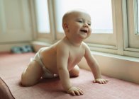 Cute baby girl in diaper laughing on window seat — Stock Photo