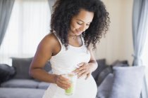 Счастливая беременная женщина пьет зеленый смузи — стоковое фото