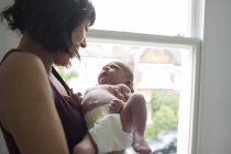 Mother holding cute newborn baby boy at window — Stock Photo