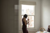 Mother holding innocent newborn baby boy at window — Stock Photo