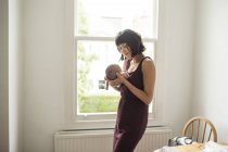 Mother holding newborn baby son at window — Stock Photo