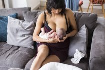 Mãe amamentando bebê recém-nascido filho no sofá — Fotografia de Stock