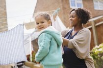 Portrait happy girl helping pregnant mother hang laundry on clothesline — Stock Photo