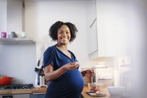 Portrait happy pregnant woman eating in kitchen — Stock Photo