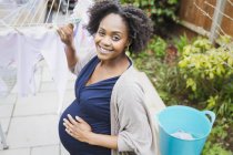 Portrait happy pregnant woman hanging laundry on clothesline — Stock Photo