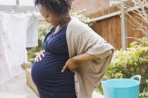 Щаслива вагітна жінка висить прання на лінії одягу — стокове фото