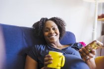 Портрет щаслива вагітна жінка п'є чай і використовує смартфон — стокове фото