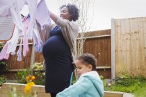 Pregnant woman with daughter hanging laundry on clothesline — Stock Photo