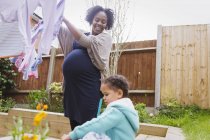 Glückliche schwangere Frau mit Tochter hängt Wäsche an Wäscheleine — Stockfoto