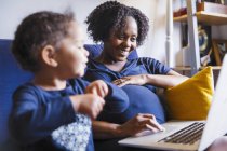 Happy pregnant woman with daughter using laptop on sofa — Stock Photo