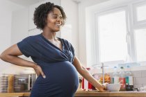 Happy pregnant woman eating in kitchen — Stock Photo