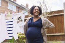Щаслива вагітна жінка висить білизну на лінії одягу в саду — стокове фото